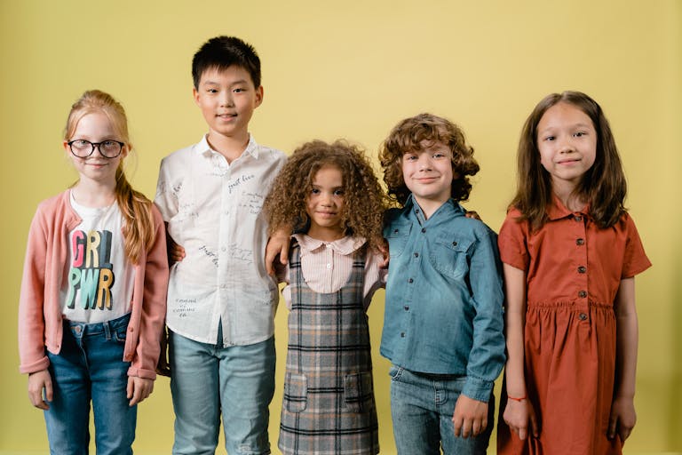 Five diverse children smiling against a yellow background in a studio setting.